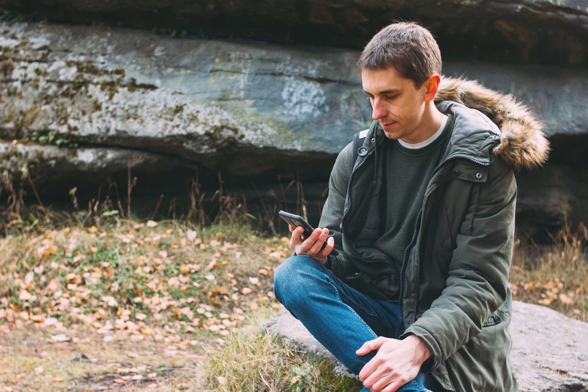 Young male traveler in khaki parka jacket with backpack looks at the route in his mobile phone