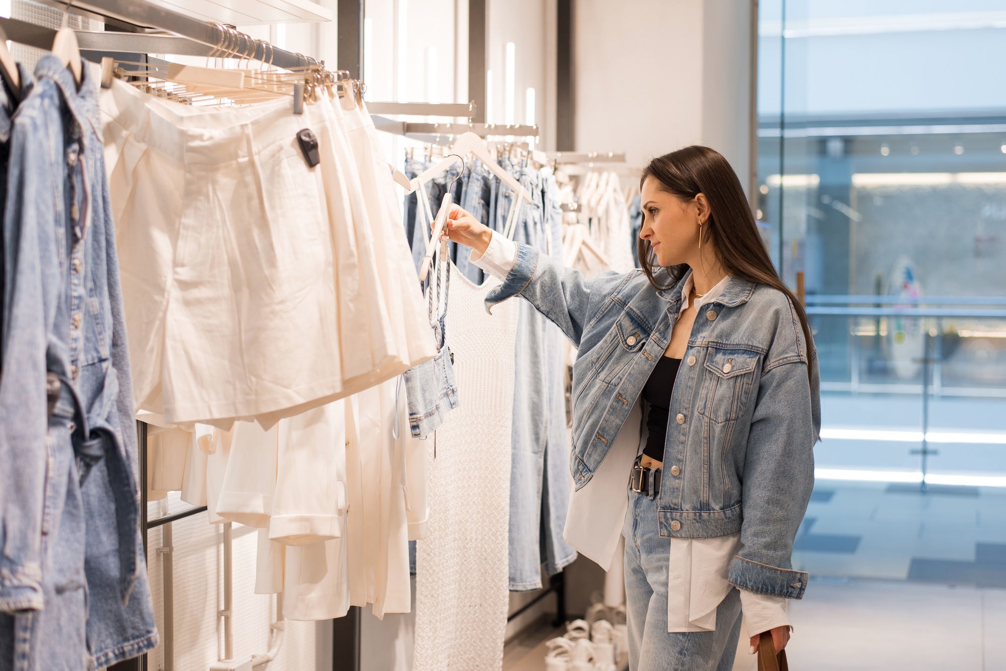 Young oman Stands in a Fashion Store, Carefully Choosing Clothing Items to Buy